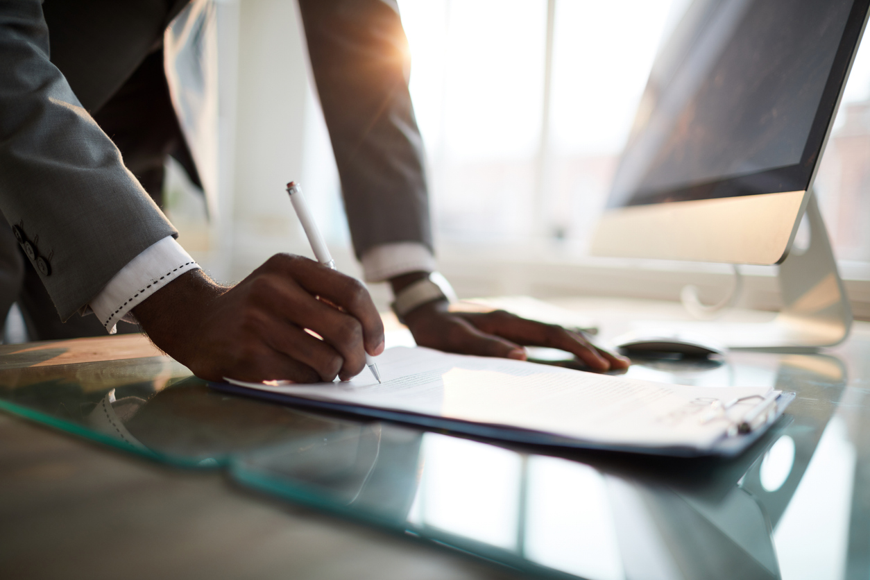 A person leans over a desk, writing on a document.