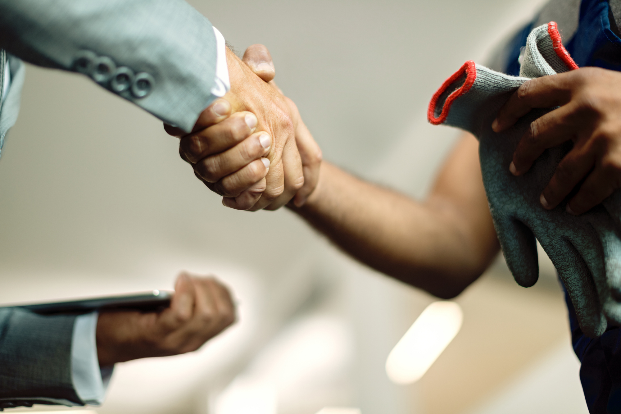 A person in a suit jacket and a person holding work gloves shake hands