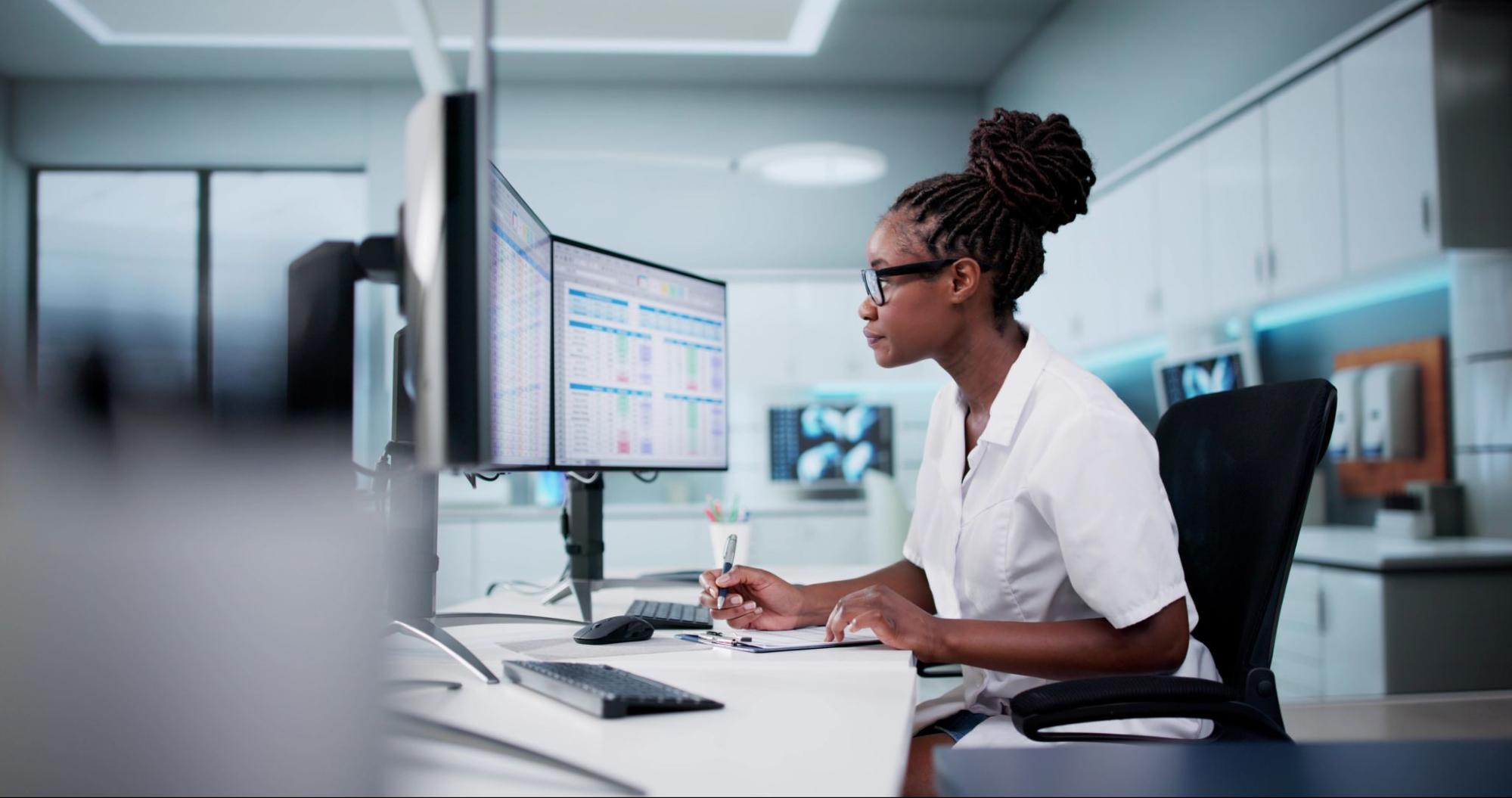 A healthcare professional updates data on a computer at her desk.