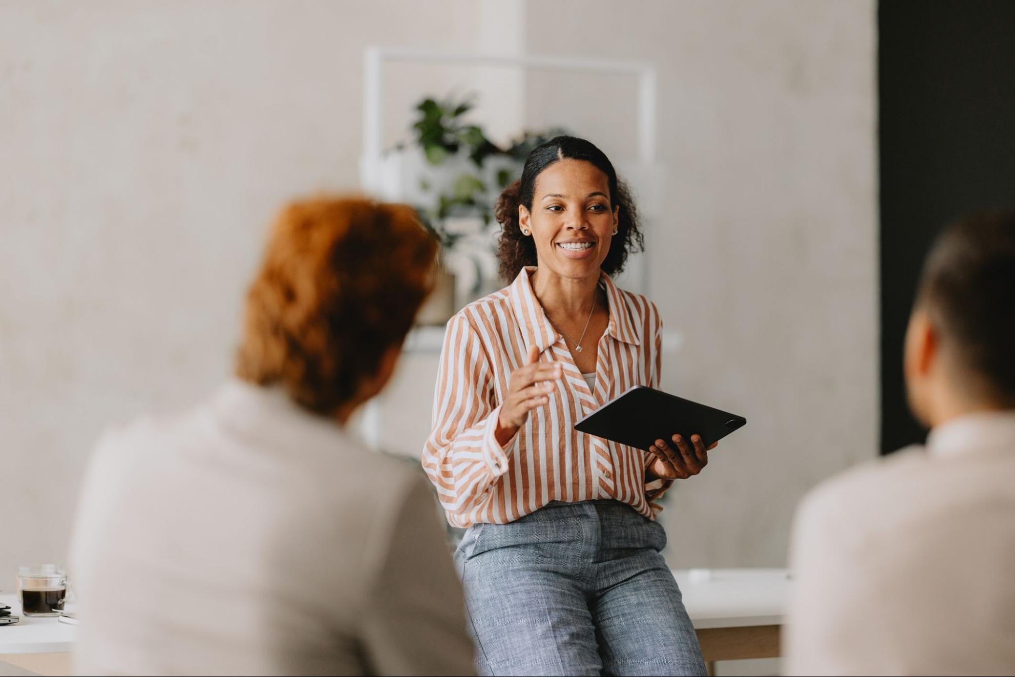 A businesswoman presents in a meeting with a smile as others listen attentively